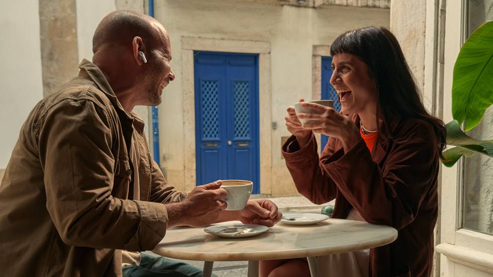 A man wearing an AirPods Pro 3 earbud while sharing coffee with a friend